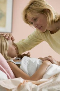 sick kid in bed while mom checks for fever